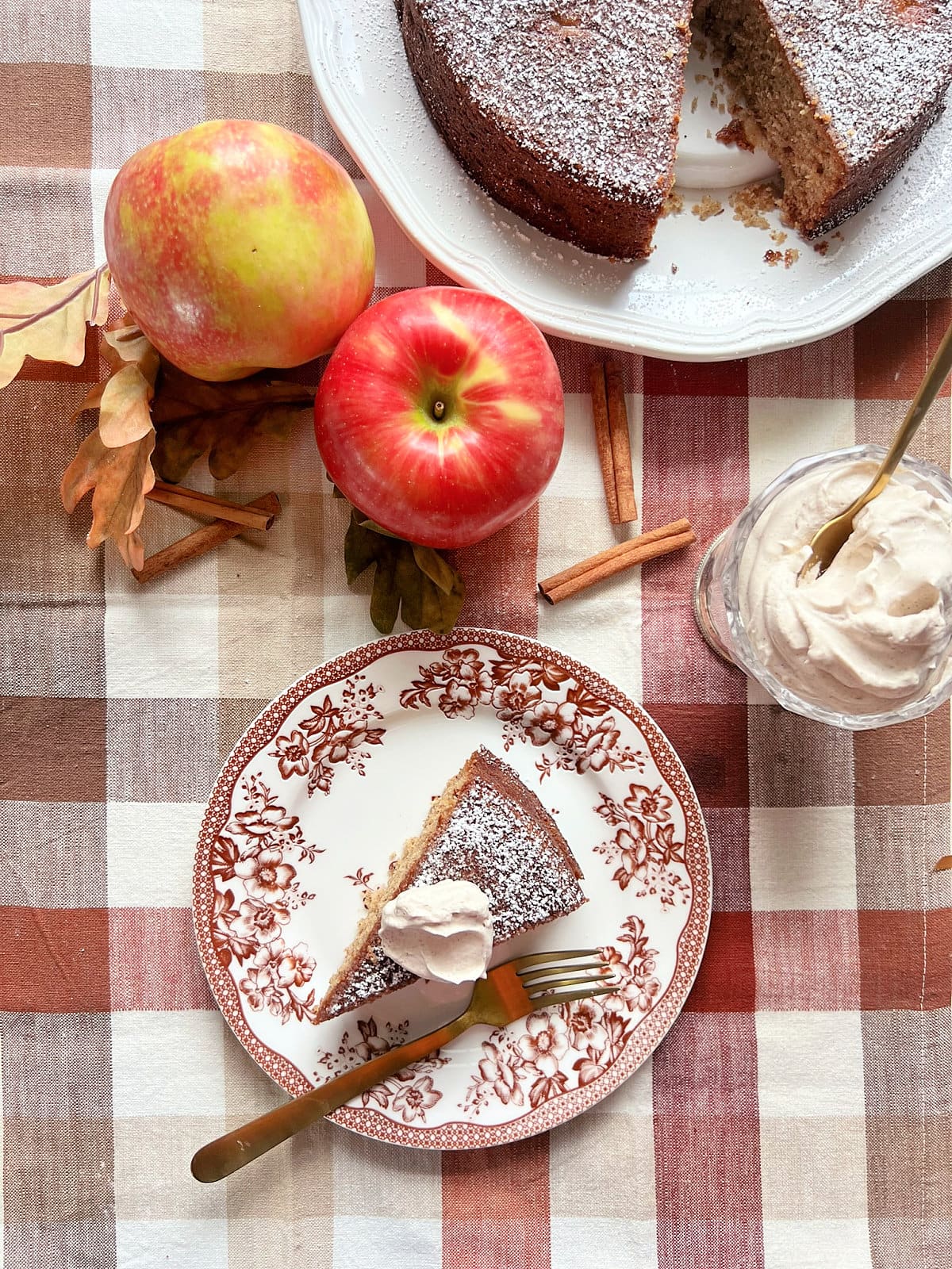 An overhead shot of a slice of apple spice cake on a plate surrounded by seasonal decor.