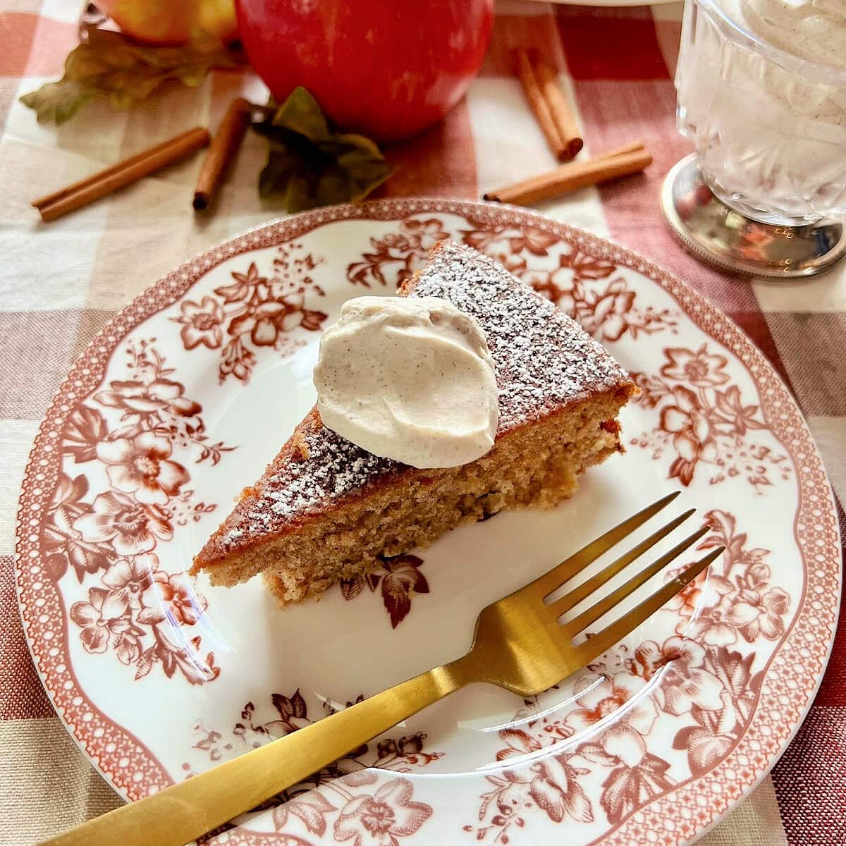 A slice of apple spice cake with a dollop of cinnamon whipped cream on a seasonal plate.