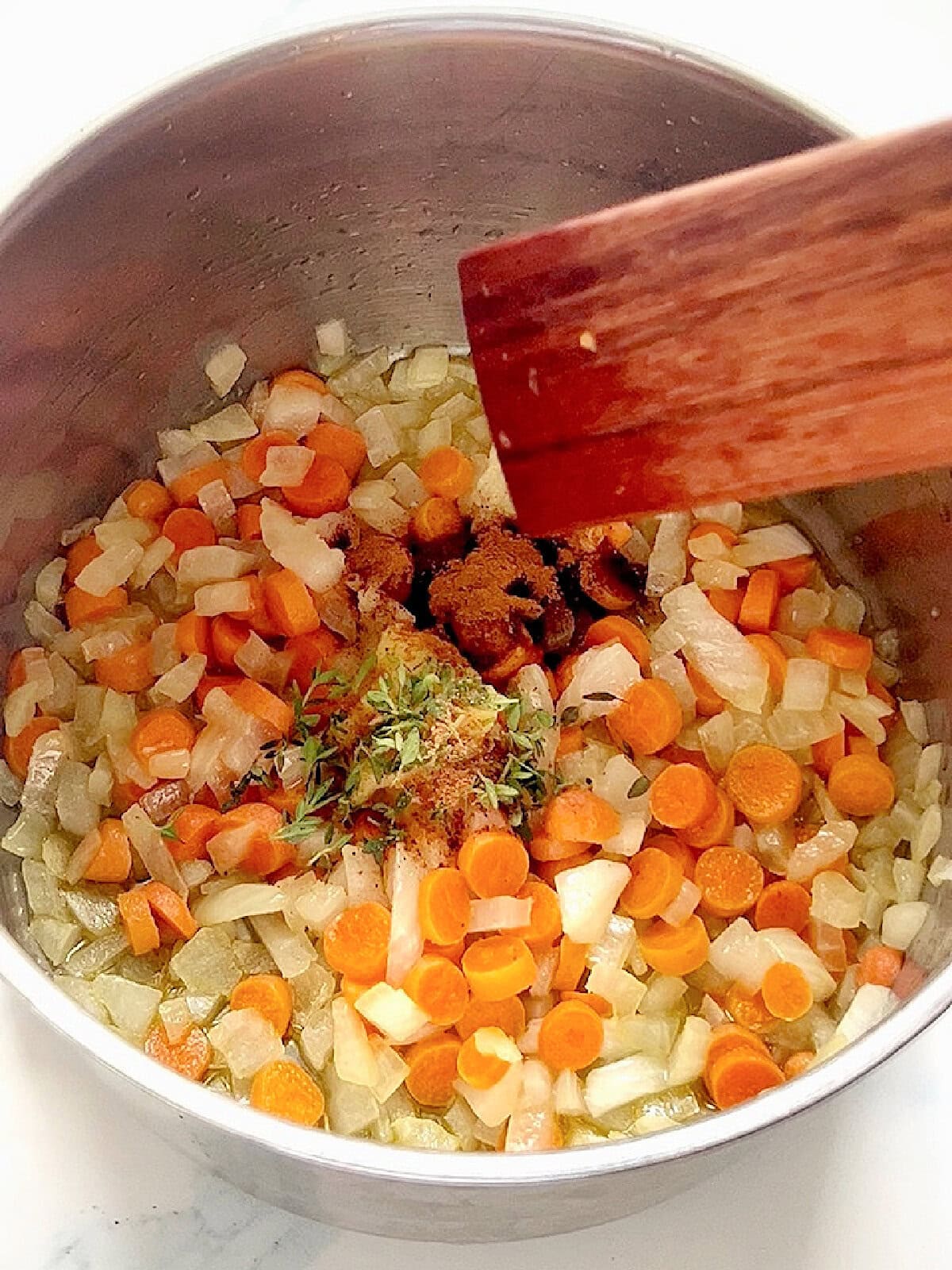 Sautéing onions, carrots, thyme, cinnamon and nutmeg in a pot.