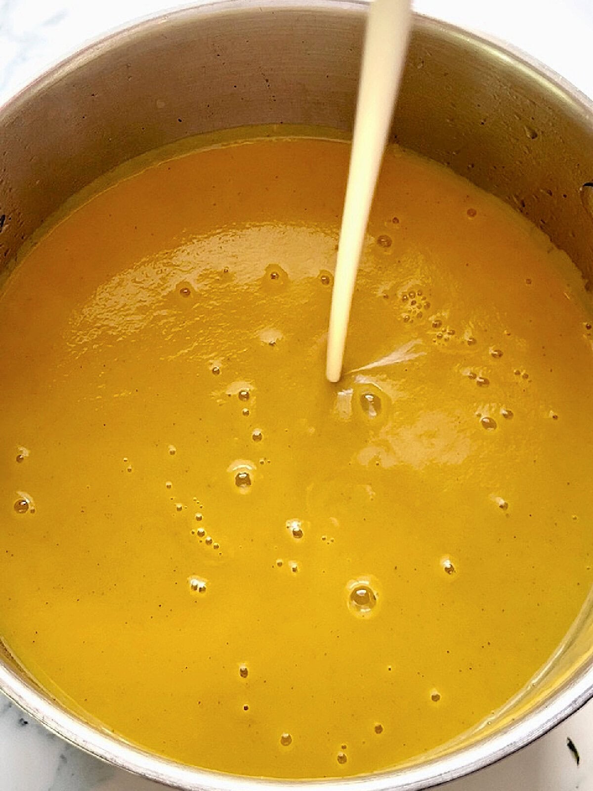 Adding a splash of heavy cream to a pot of butternut squash soup.