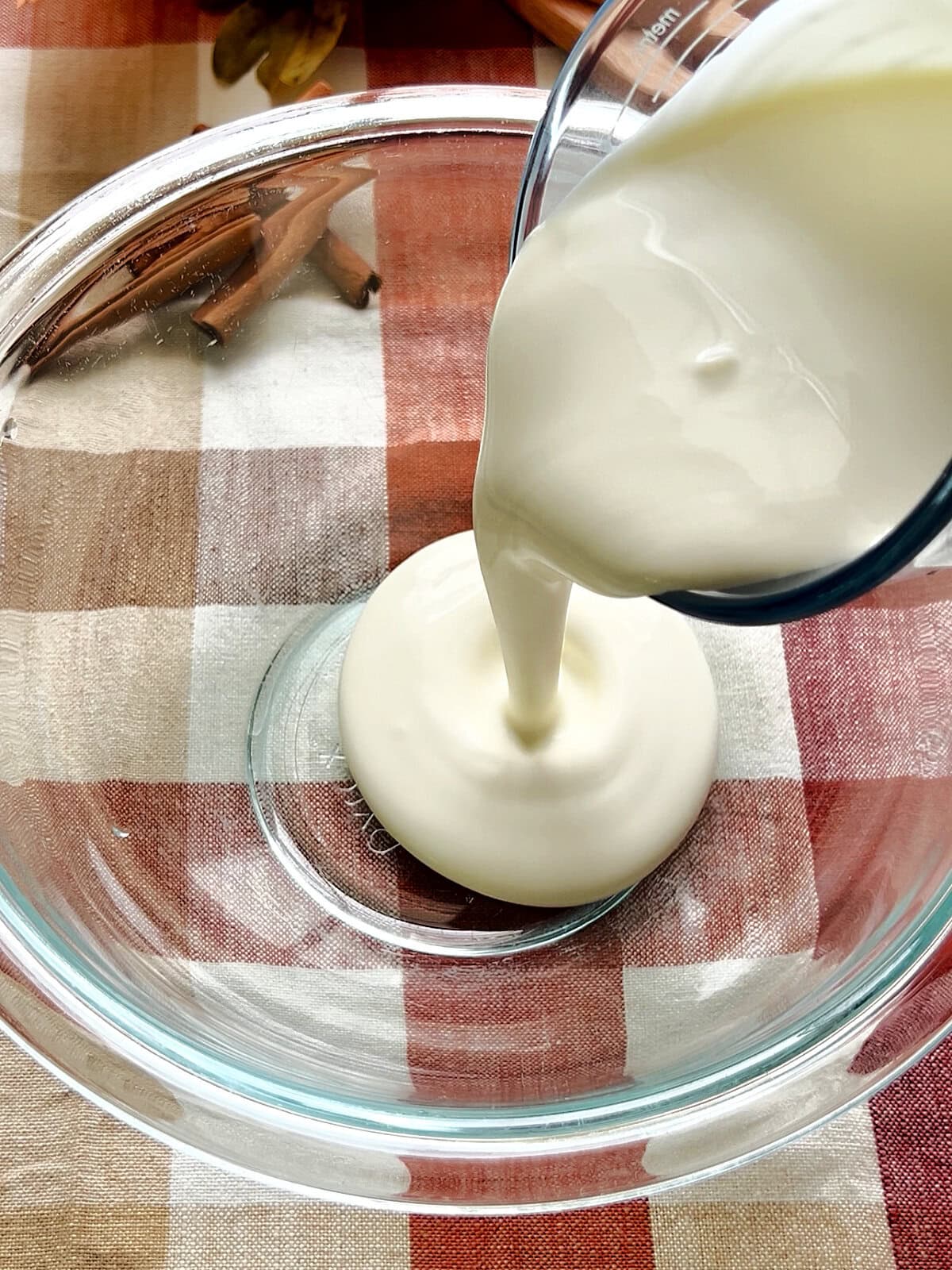 Pouring chilled heavy cream into a chilled glass bowl to make Cinnamon Whipped Cream.
