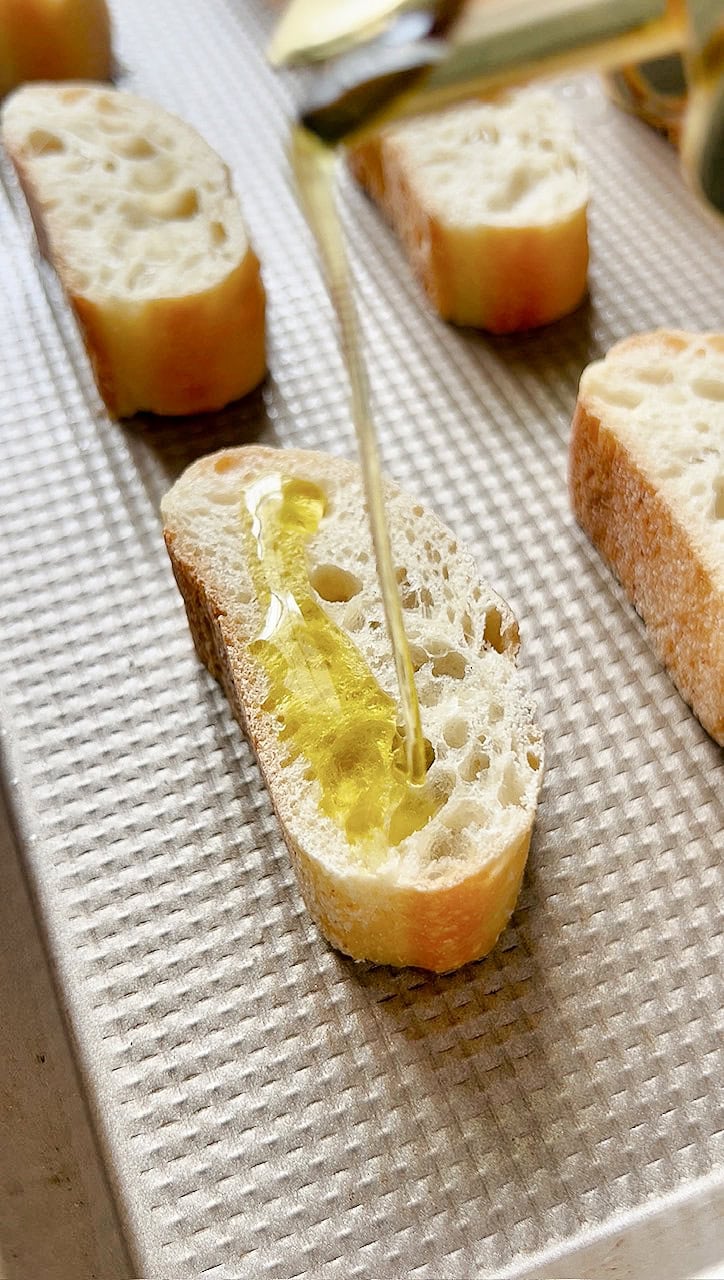 Pouring olive oil on a slice of baguette for crostini.