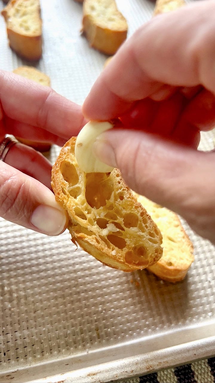 Rubbing raw garlic on a warm, toasted piece of baguette for garlic crostini.