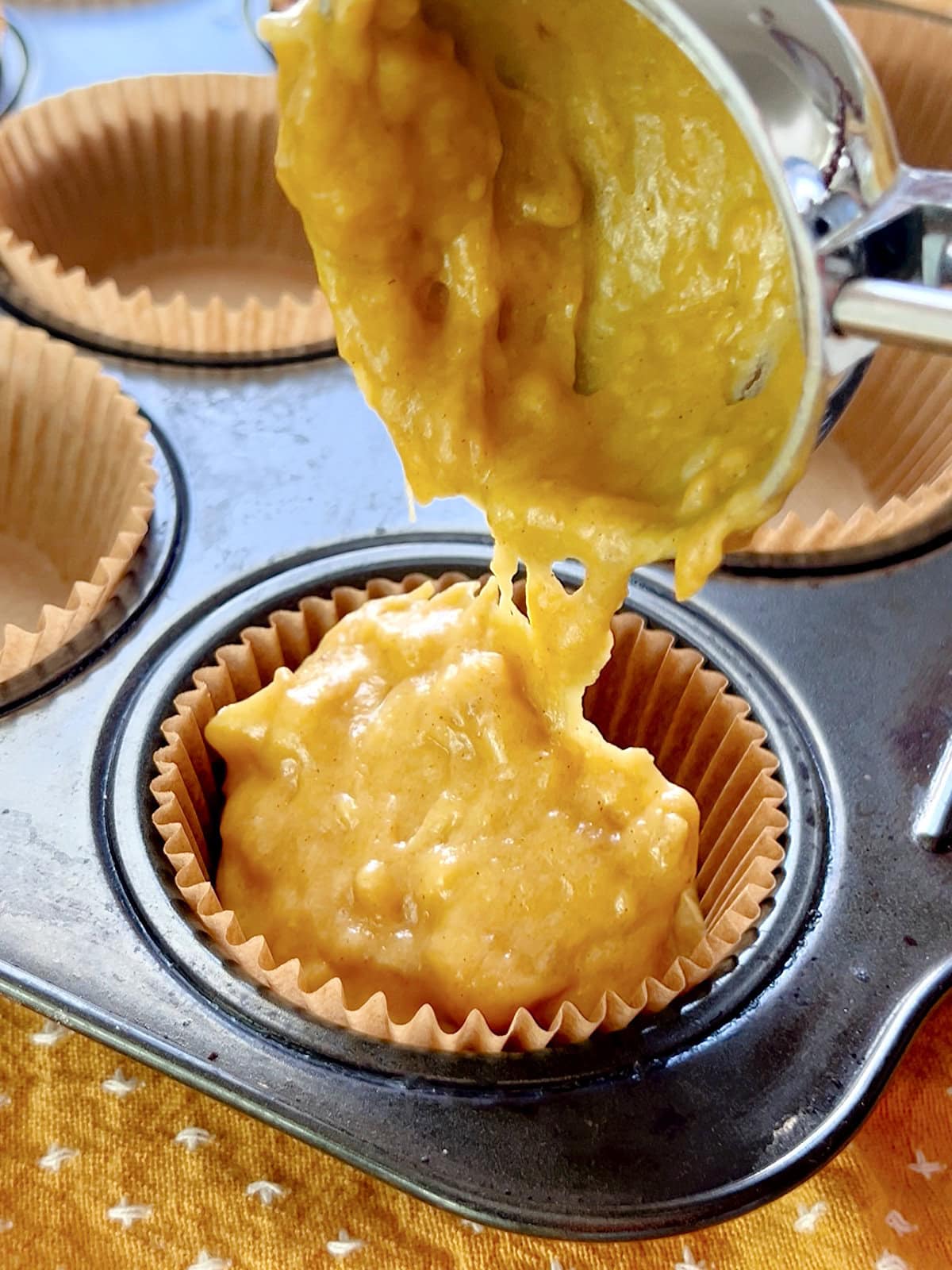 Batter for pumpkin banana bread muffins being scooped into a muffin tin.