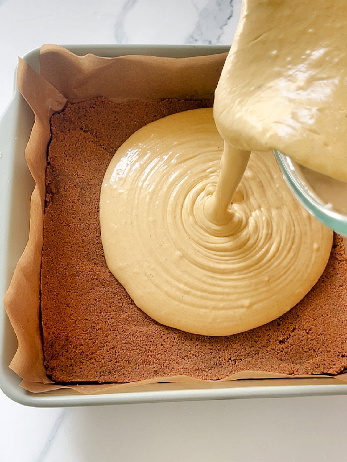Pouring pumpkin cheesecake batter over cinnamon graham cracker crust in pan.