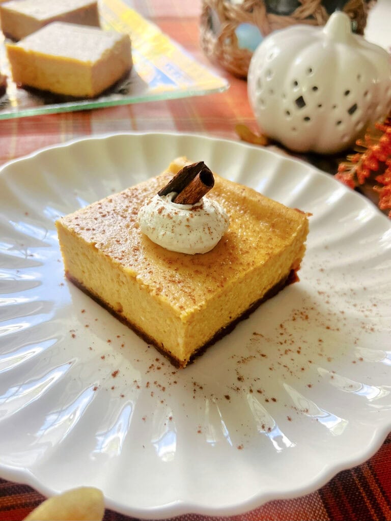 A Pumpkin Cheesecake Bar on a white plate sprinkled with pumpkin spice.