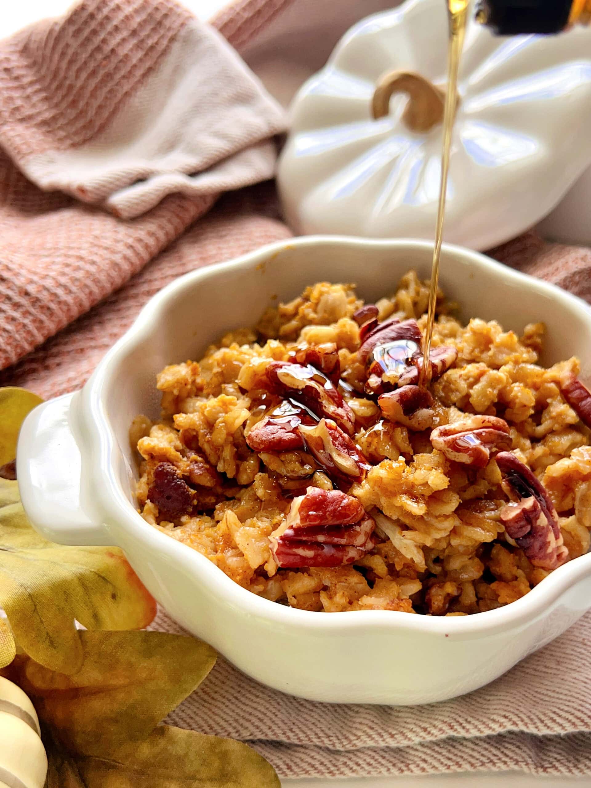 Maple syrup being poured over a pumpkin shaped ramekin of Baked Pumpkin Oatmeal.