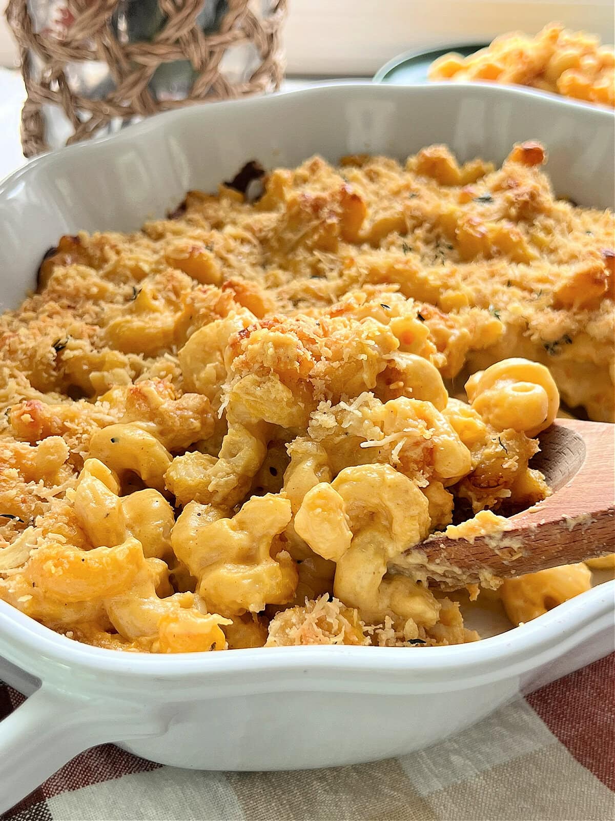 A close up of a spoonful of Pumpkin Mac & Cheese being served from a white baking dish.
