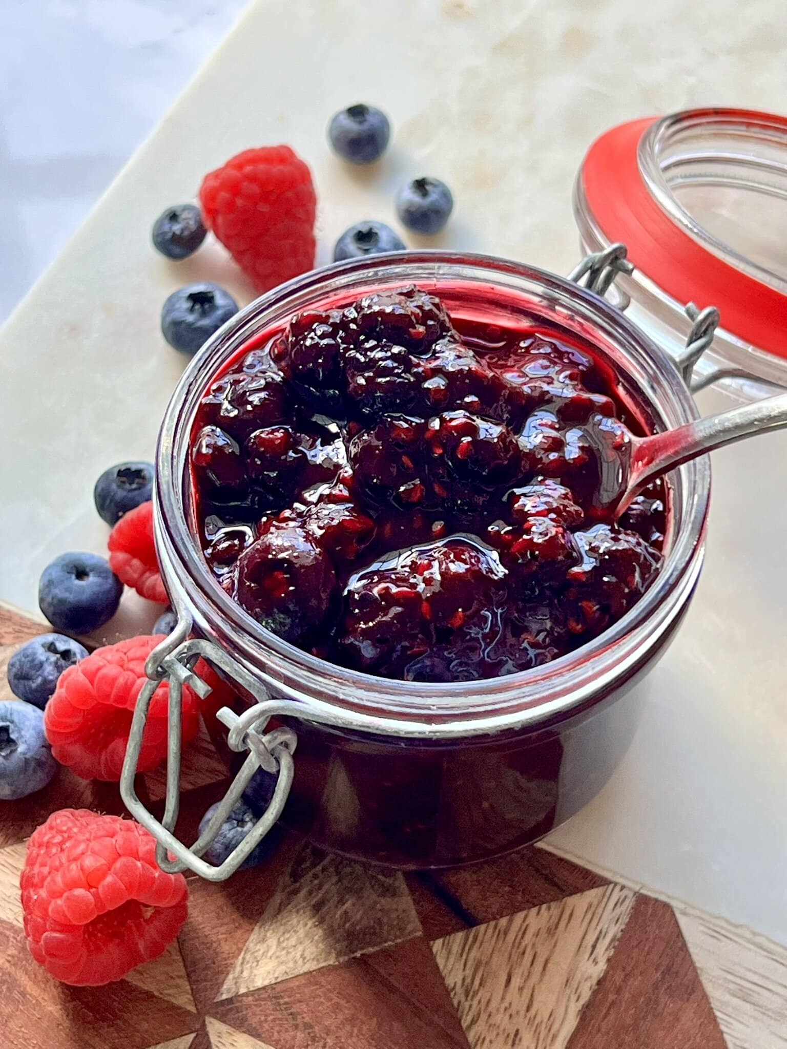 Mixed Berry Compote in a glass container surrounded by berries.