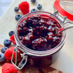 Mixed Berry Compote in a glass container surrounded by berries.
