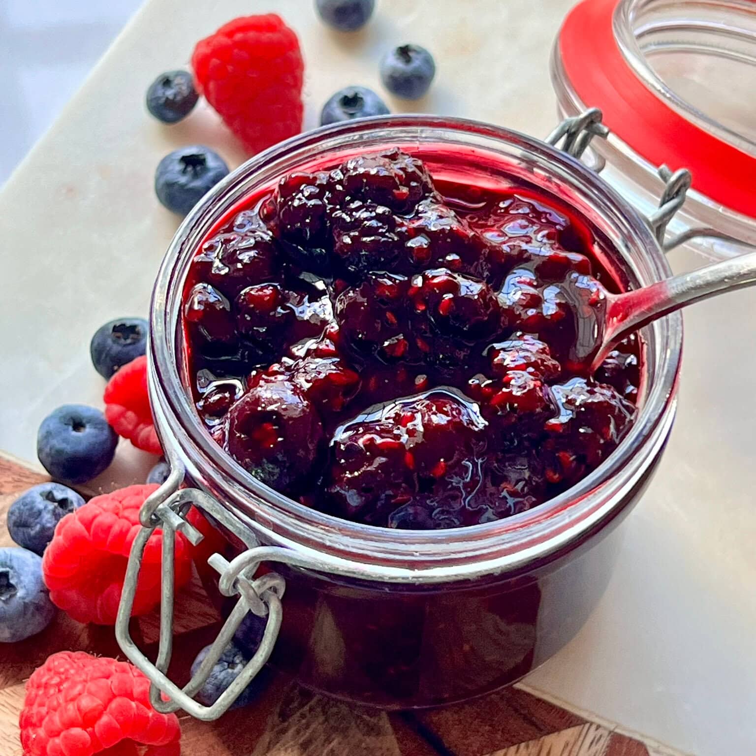 Mixed Berry Compote in a glass container surrounded by berries.
