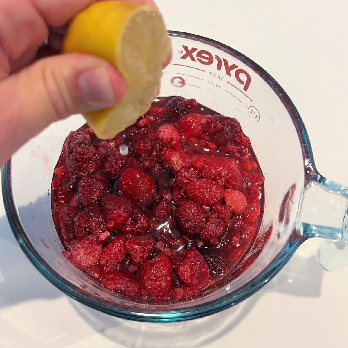 Adding lemon juice to frozen raspberries and simple syrup in a measuring cup for raspberry sorbet.