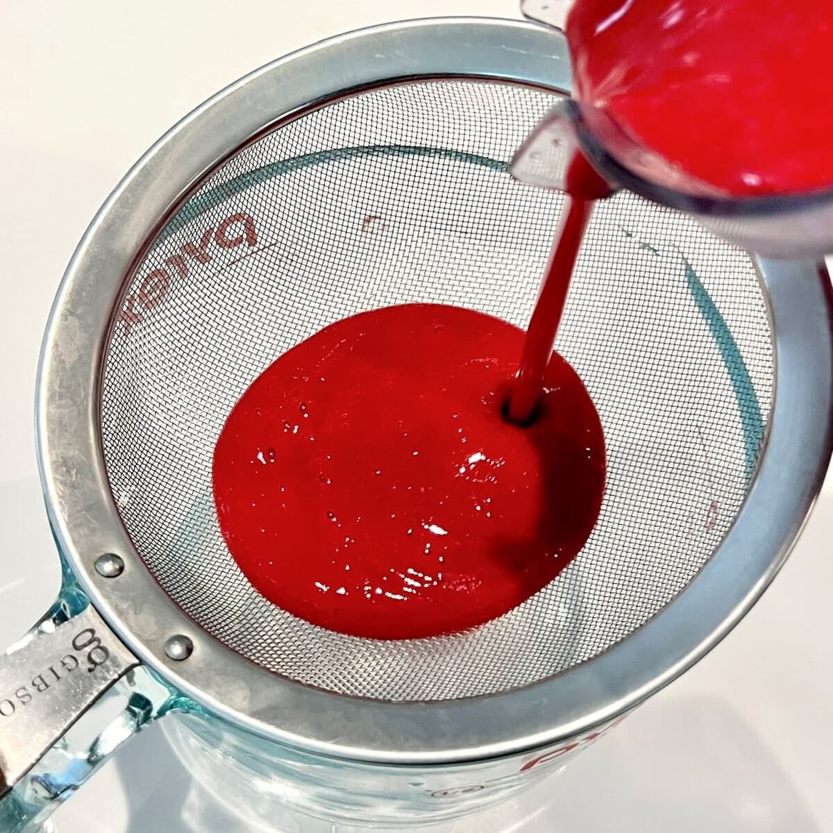 Pouring blended raspberry mixture for raspberry sorbet through a fine mesh sieve.