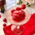 A scoop of raspberry sorbet served in a champagne coupe topped with prosecco.