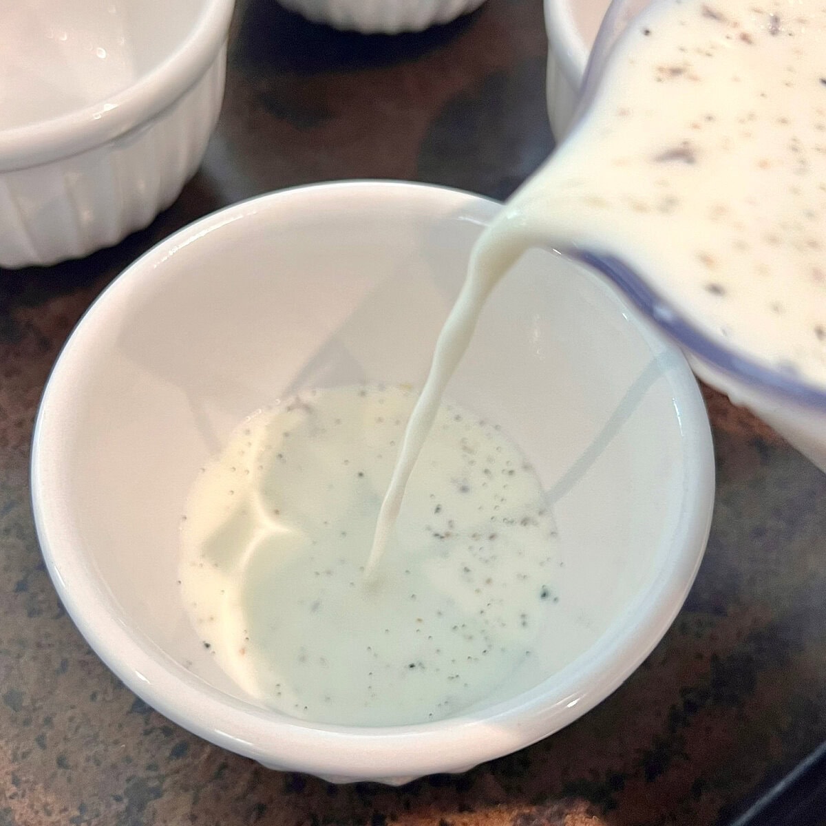 Pouring cream mixture for Vanilla Bean Panna Cotta into a ramekin.