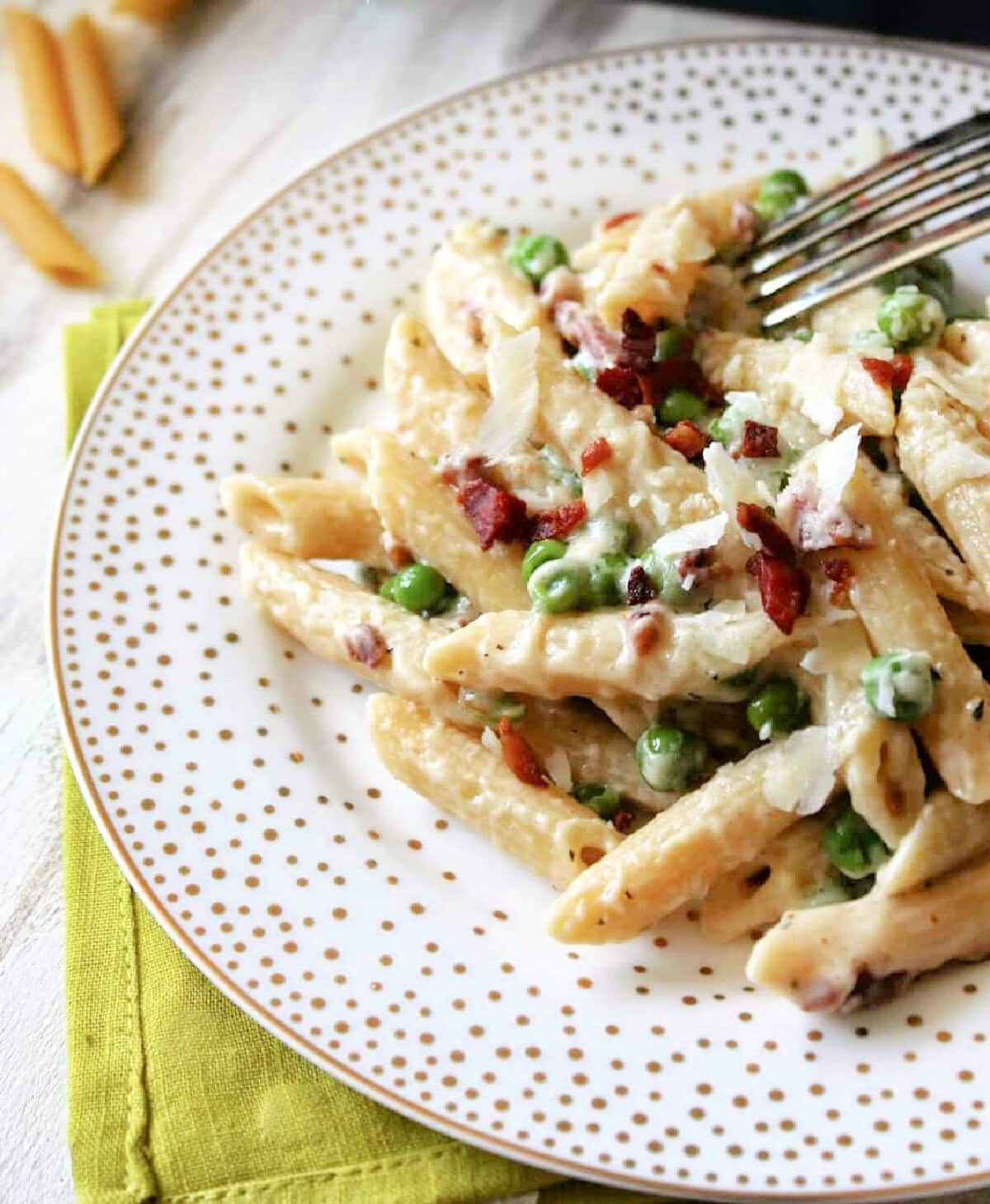 Creamy Penne Pasta with Pancetta & Peas on a white plate with gold dots.