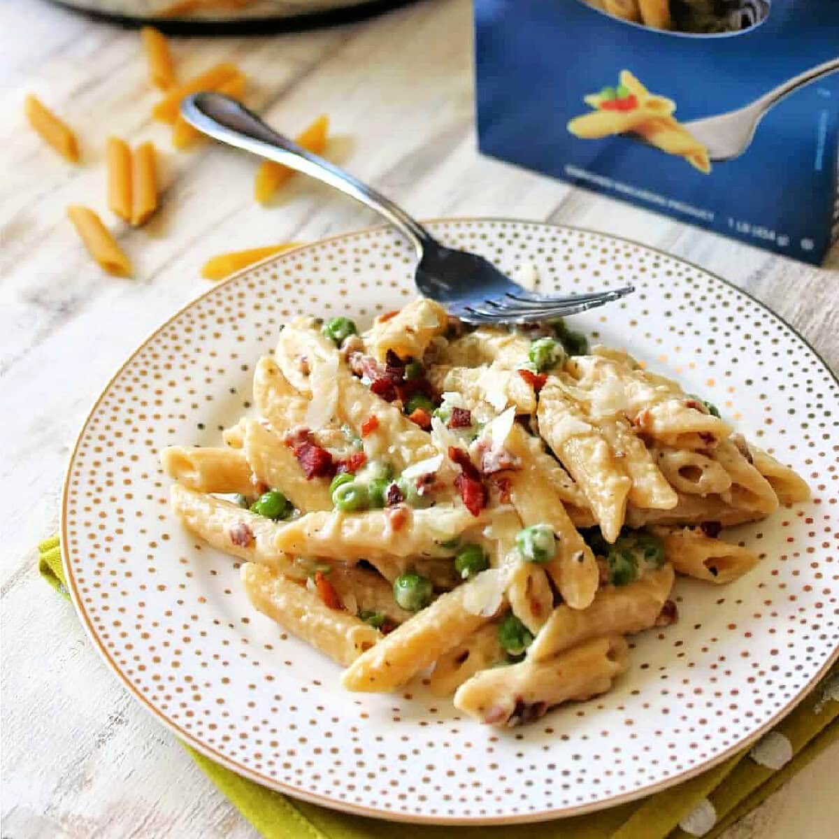 Close up of Creamy Penne Pasta with Pancetta & Peas on a white plate with gold dots.