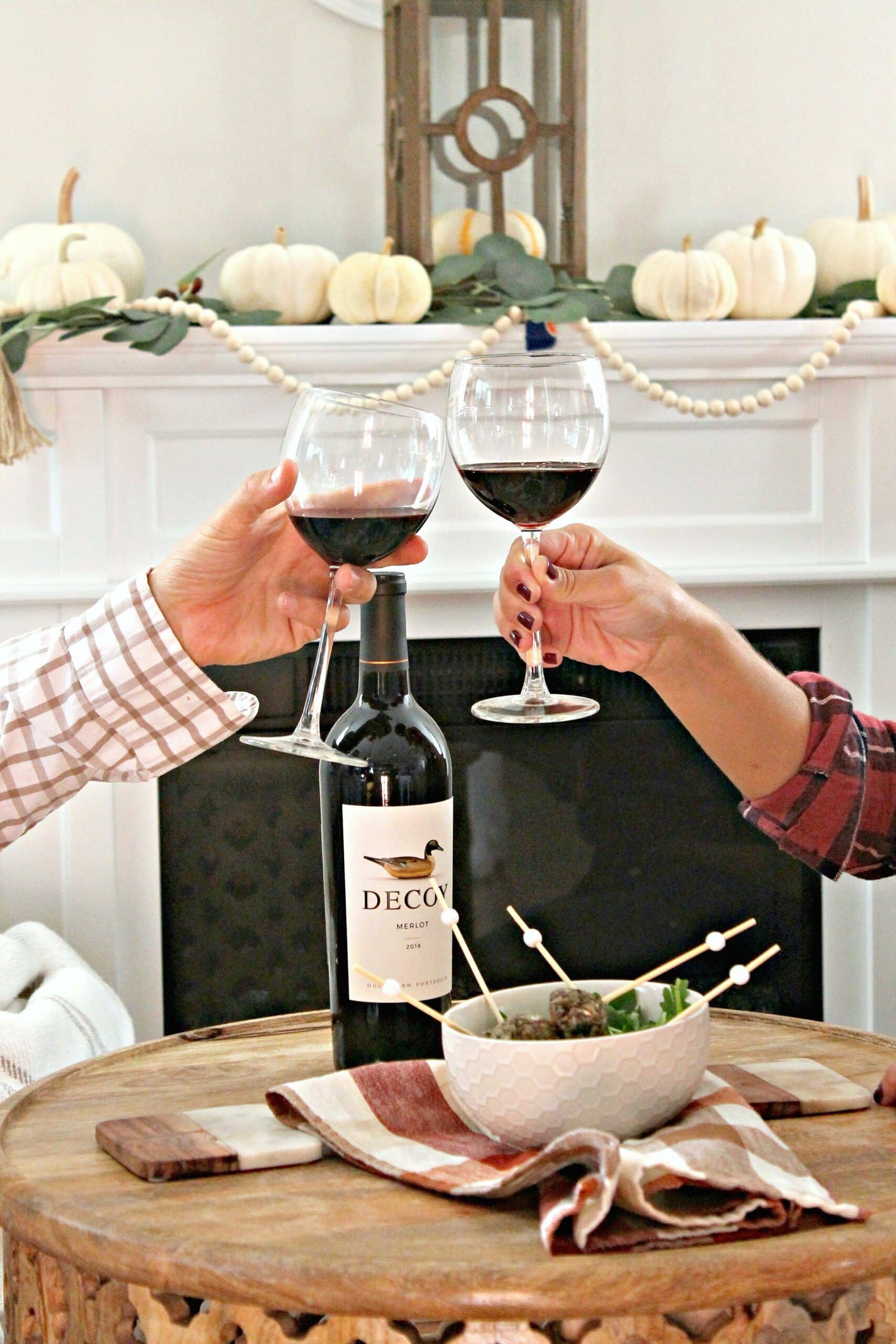 Toasting of glasses filled with red wine in front of a fall decorated mantle.